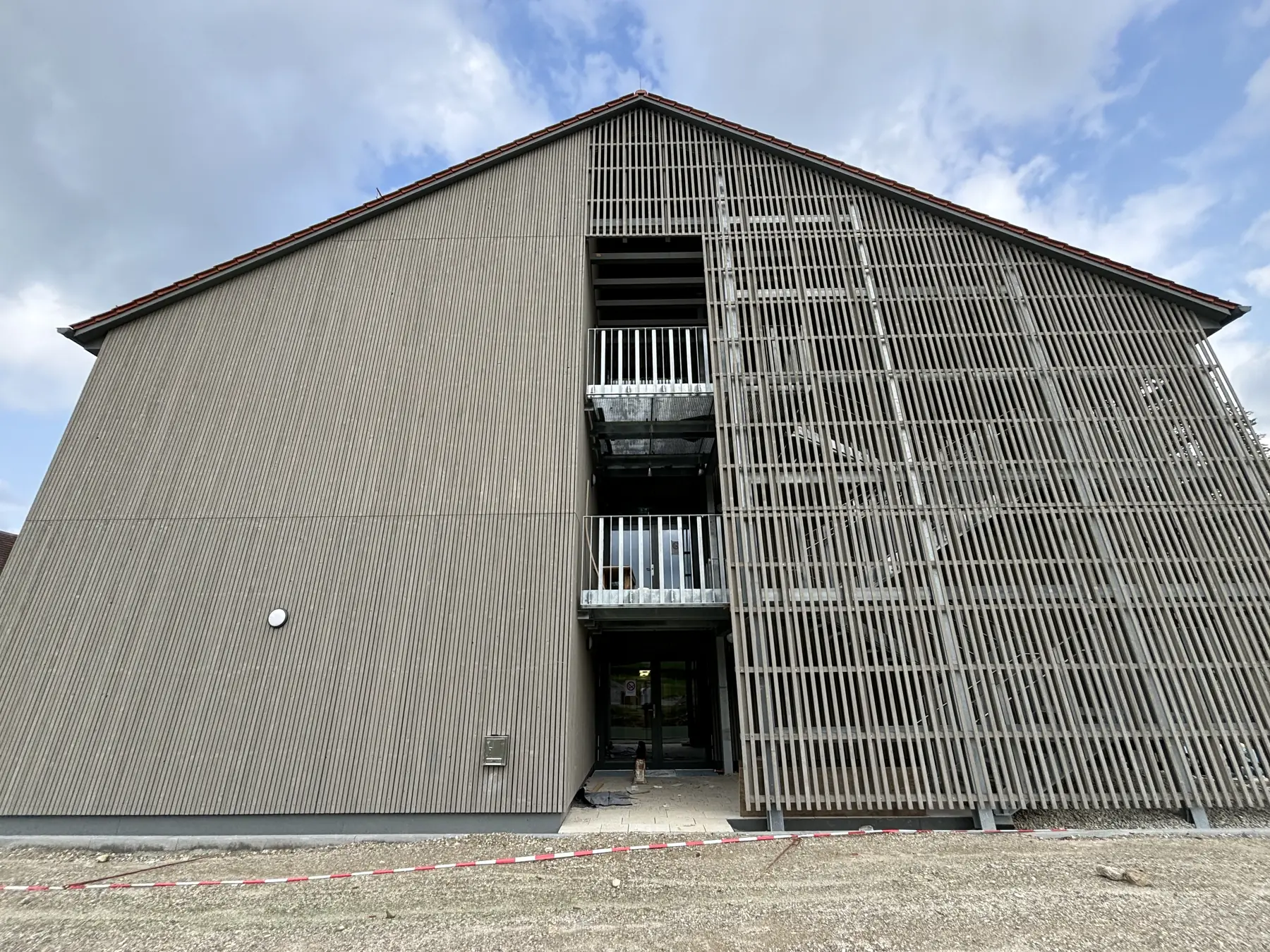 Sporthalle in Holzbauweise, davor ein Schirm aus vertikalen Latten